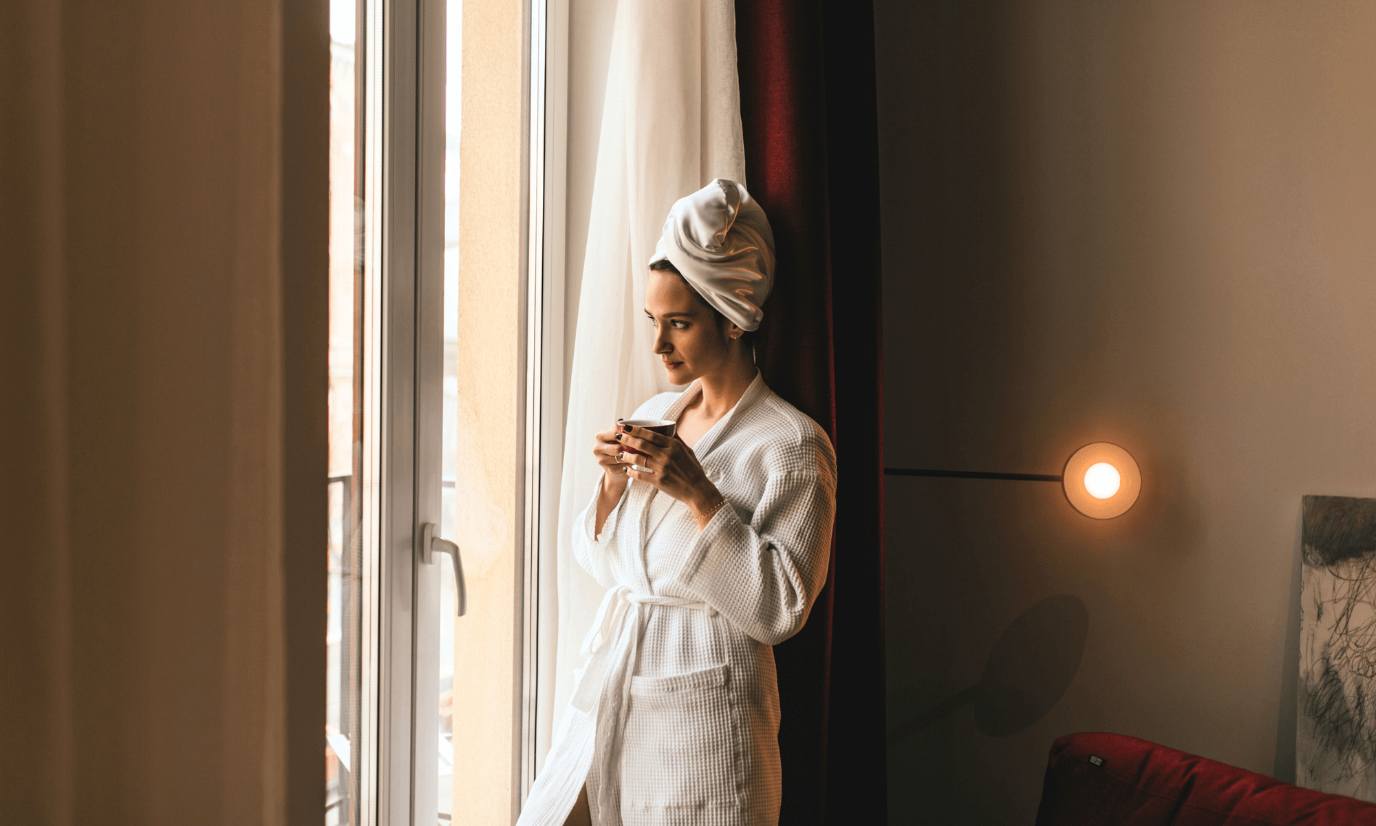 Kobieta relaksująca się z kawą przy hotelowym oknie."